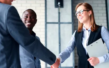 O que é o seguro de crédito interno? Na imagem, dono de empresa apertando a mão de uma corretora após a contratação do seguro contra inadimplência de clientes.