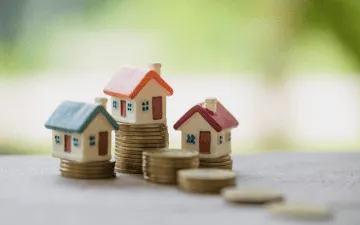 Casas em miniatura com moedas ao redor em alusão à importância do seguro fiança locatícia