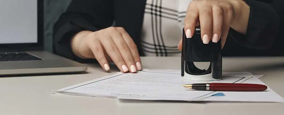 O que é seguro garantia administrativo? Na imagem, mulher carimba papelada em alusão à importância do seguro garantia administrativo no cenário fiscal