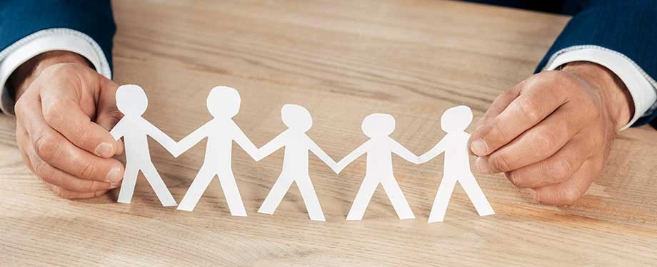 Qual o valor da indeniza&ccedil;&atilde;o no seguro de vida em grupo? Na imagem, pessoa segurando bonecos de papel em alus&atilde;o ao seguro de vida coletivo, cujo valor da indeniza&ccedil;&atilde;o depende das condi&ccedil;&otilde;es da ap&oacute;lice contratada 