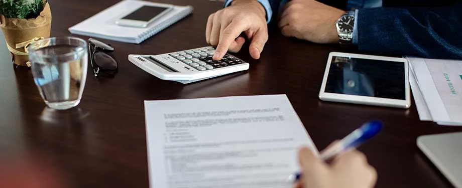 Pessoas trabalhando em uma mesa de escritório com calculadora e papeis ilustrando a ideia de seguro garantia retenção de pagamentos