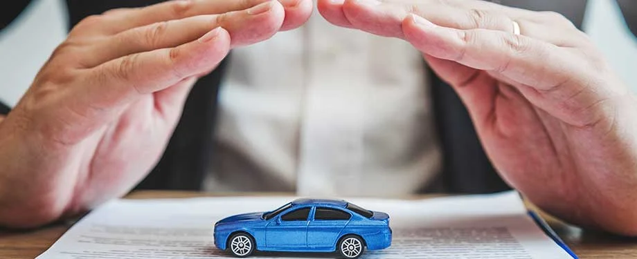 Como contratar seguro para locadoras de ve&iacute;culos? Na imagem, carro em miniatura protegido por m&atilde;os em alus&atilde;o ao seguro que protege o patrim&ocirc;nio e a continuidade dos neg&oacute;cios das locadoras de ve&iacute;culos 