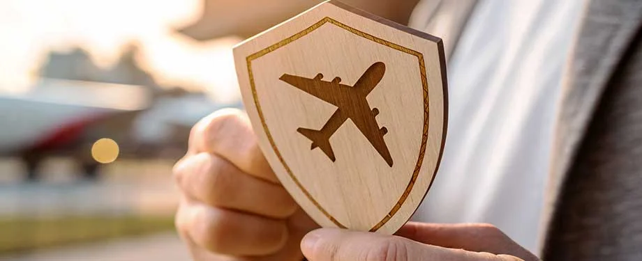 Qual o valor m&eacute;dio de um seguro viagem internacional? Na imagem, pessoa segurando escudo com s&iacute;mbolo de avi&atilde;o em alus&atilde;o ao seguro viagem internacional, cujo valor depende de muitos fatores, como destino, dura&ccedil;&atilde;o, coberturas e seguradora contratada 