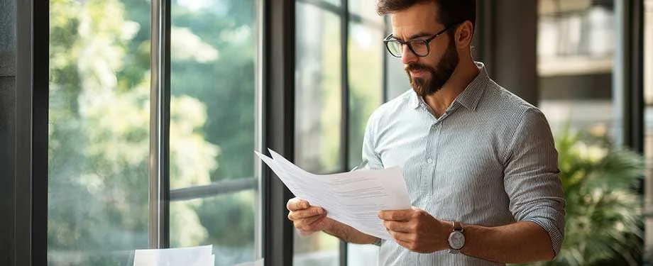 Como se d&aacute; a liquida&ccedil;&atilde;o de sinistro no seguro RCO? Na imagem, homem com papelada representa o sinistro no RCO, que pode ser acionado a partir da comunica&ccedil;&atilde;o com a seguradora 
