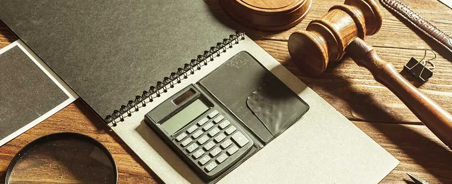 O que trata a Lei 6.830 de 1980? Na imagem, vemos caderno com calculadora e martelo da justiça ao lado, fazendo alusão aos procedimentos de cobrança determinados pela Lei de Execução Fiscal