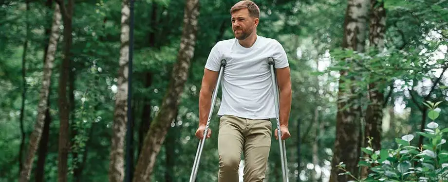 Quais são os tipos de invalidez? Na imagem, homem andando com muletas em alusão a um dos tipos de invalidez parcial