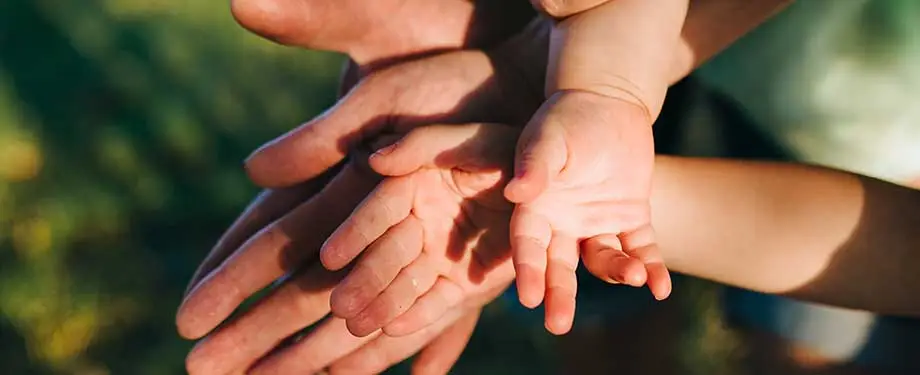 Qual é o seguro de vida mais barato? Na imagem, mãos de adultos e criança representam a possibilidade de encontrar preço de seguro de vida com bom custo benefício