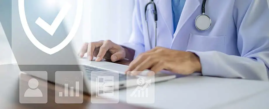 O que é responsabilidade civil do médico? Na imagem, médico digita no computador, representando que o RC profissional pode ser contratado de forma digital