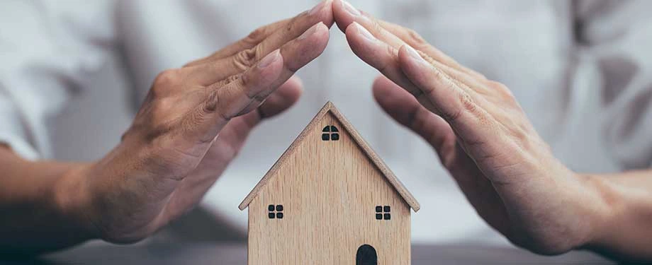 Cobertura compreensiva cobre enchente? Na imagem, pessoa cobrindo casa com as m&atilde;os em alus&atilde;o a import&acirc;ncia de contratar o seguro compreensivo residencial para trazer seguran&ccedil;a para o seu lar 