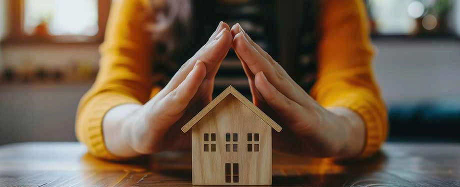 O que a cobertura compreensiva cobre? Na imagem, pessoa protegendo casa com as m&atilde;os em alus&atilde;o ao seguro compreensivo residencial, que tem coberturas adicionais como colis&atilde;o, furto e roubo 