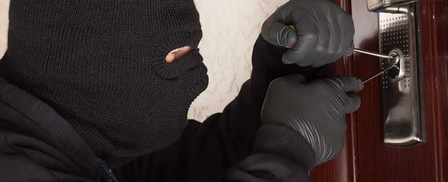 Quais as coberturas adicionais do seguro residencial roubo e furto? Na imagem, pessoa arrombando porta representa seguro residencial roubo e furto, que tem coberturas adicionais como incêndios e vendavais