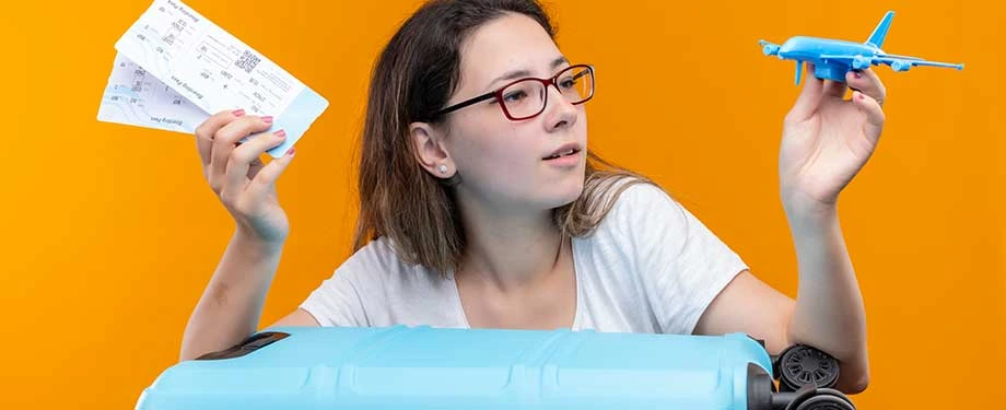 Quais as coberturas de seguro para viagem? Na imagem, mulher segura avião de brinquedo e passagens aéreas em alusão ao seguro viagem, que costuma cobrir, principalmente, despesas médicas e hospitalares