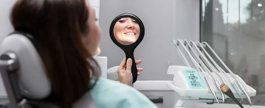 Paciente sentada na cadeira observa o sorriso no espelho após procedimento com dentista, ilustrando a ideia de seguro para clínica odontológica