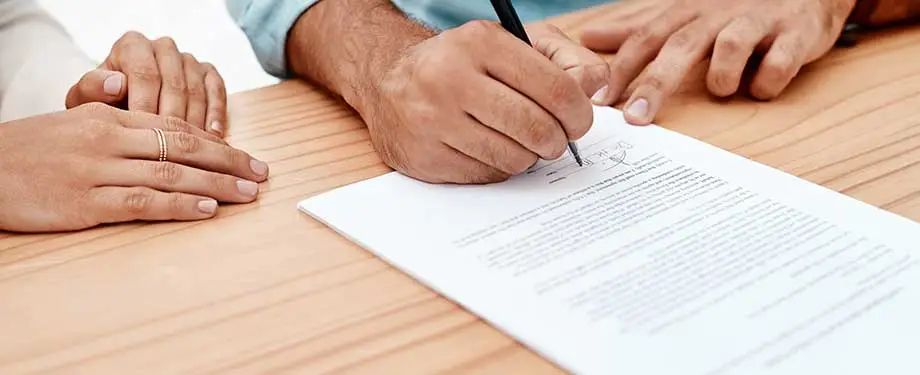 Seguro garantia contratual como funciona? Na imagem, mão masculina assina apólice de seguro garantia contratual, que serve para assegurar as obrigações estabelecidas por meio de um contrato
