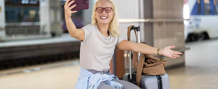 Como funciona o seguro viagem Assist Card? Na imagem, mulher tira foto sorrindo em aeroporto representando a segurança de uma apólice de viagem da Assist Card