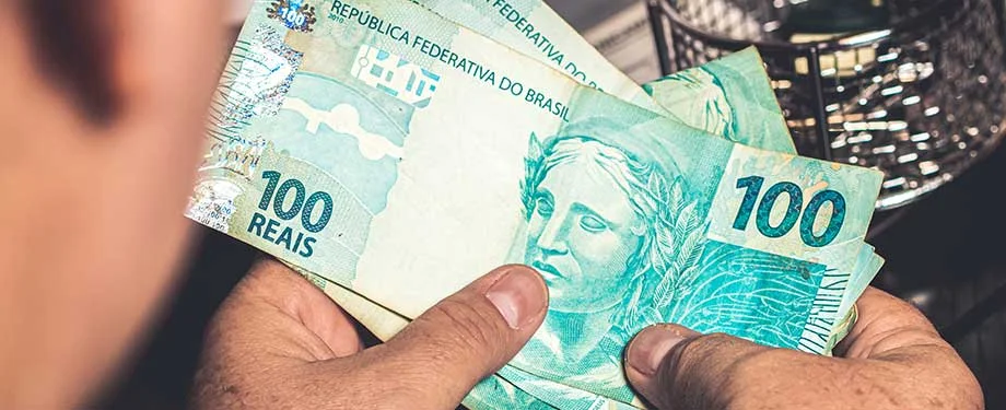 Tr&ecirc;s notas de cem reais nas m&atilde;os de um homem em alus&atilde;o ao seguro prestamista empresarial