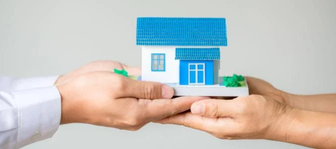 o-que-e-fianca-empresarial O que é fiança empresarial? Na imagem, duas pessoas segurando uma casa em miniatura em alusão aos benefícios da fiança empresarial e como funciona essa garantia.